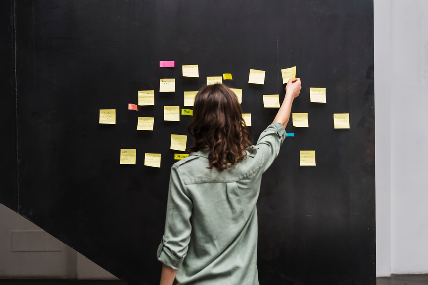 image of a young woman placing colorful sticky notes on a blackboard