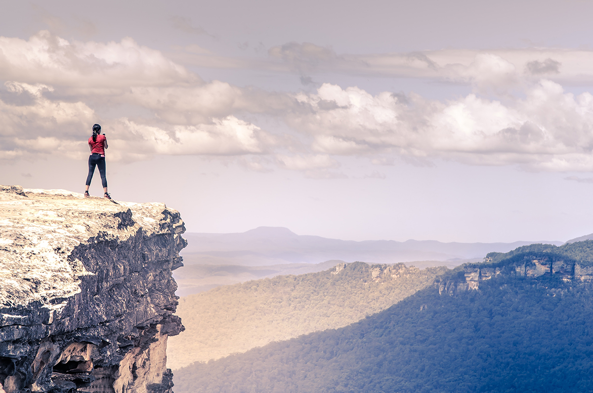 image of a woman standing on a cliff looking over hills