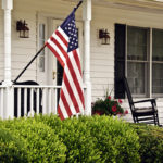 American flag on front porch of a white house with black shutters