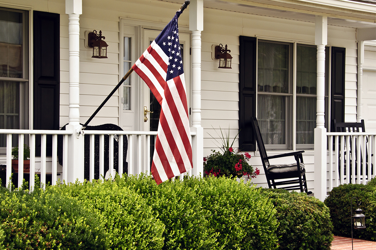 American flag on front porch of a white house with black shutters