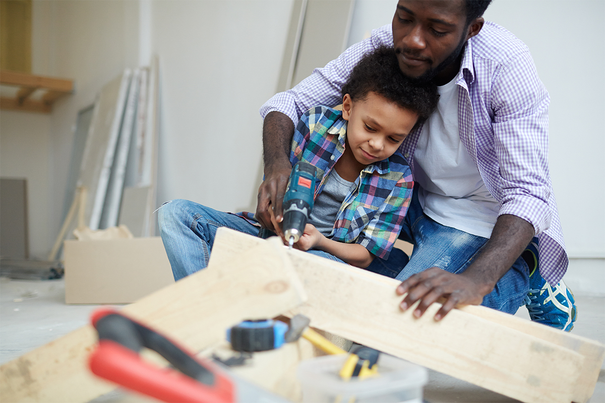 a father helps a young son operate a cordless drill