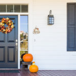 brown front door with autumnal wreath and pumpkins