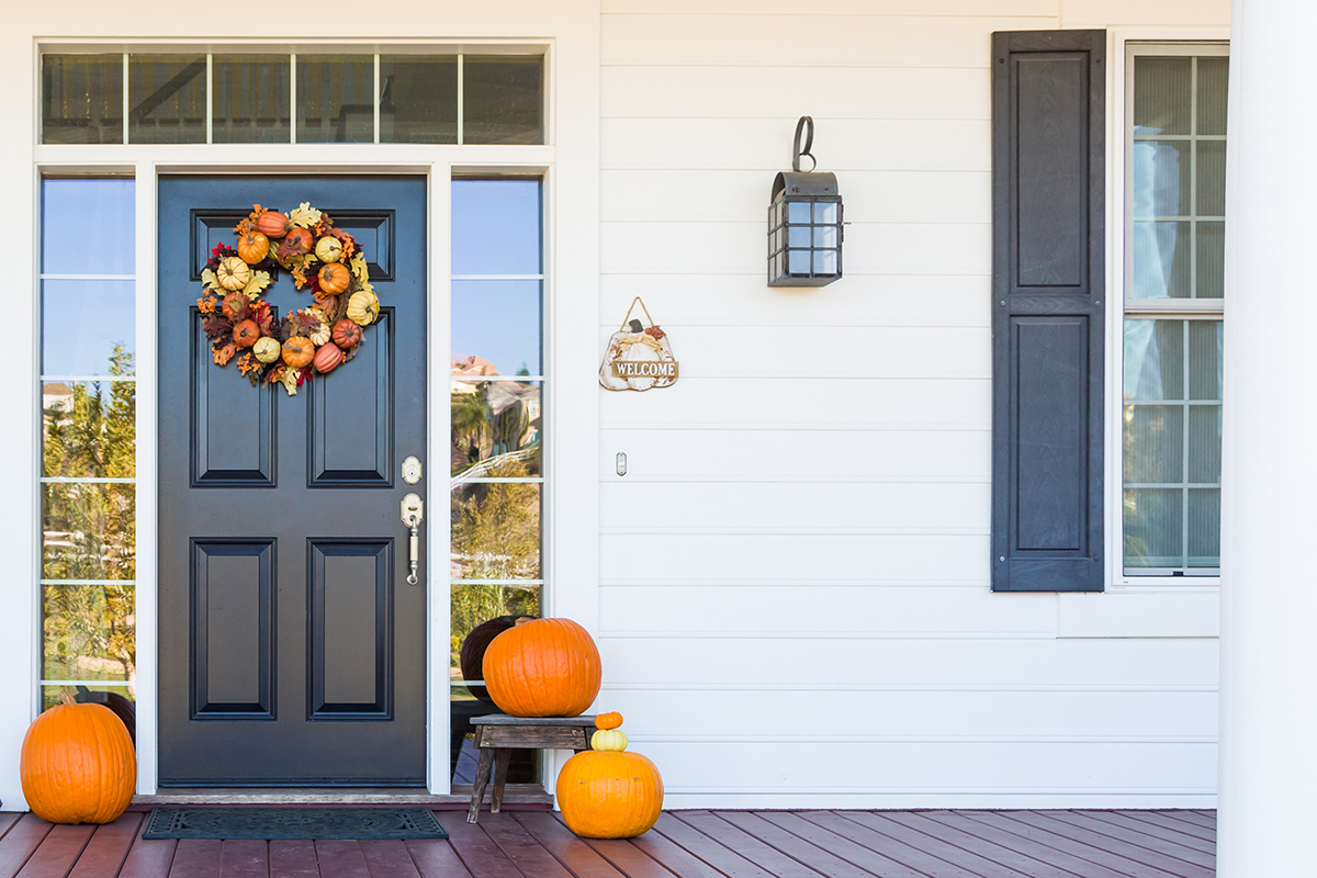 brown front door with autumnal wreath and pumpkins