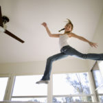 happy young girl jumps in mid-air with ceiling fan in background