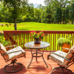 deck chairs and table sit on deck overlooking beautiful green lawn