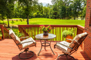 deck chairs and table sit on deck overlooking beautiful green lawn