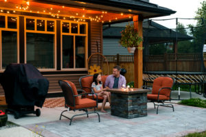 father and young daughter sit at firepit in back yard under outdoor lights