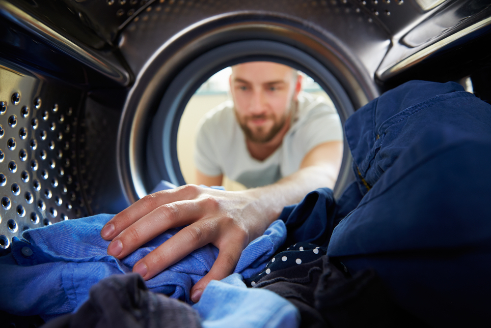 young man reaches into dryer for clothing