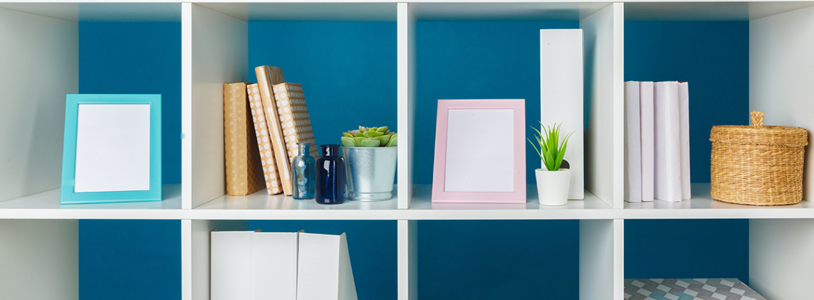 blue pained background with a white multi square shelf with various office supplies, pictures, and fake plants