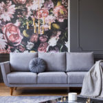 a living room with a gray couch and a floral wallpaper