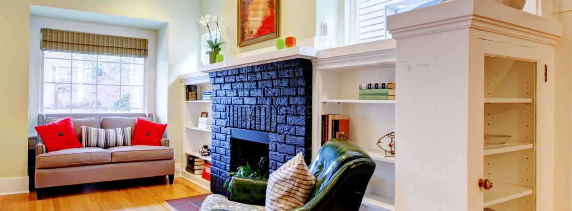 A living room with a fire place, green chair, brown couch, and cabinets
