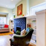 A living room with a fire place, green chair, brown couch, and cabinets