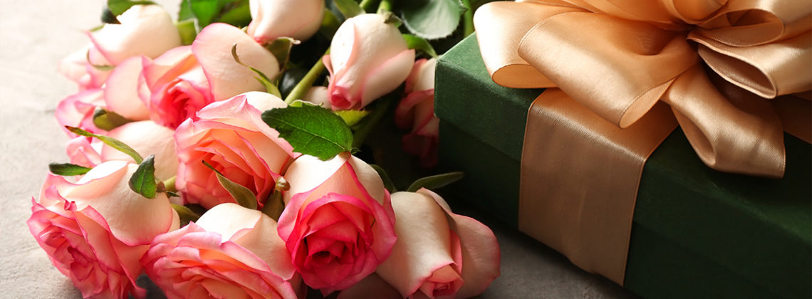 pink roses next to a green gift box with a large gold bow