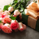 pink roses next to a green gift box with a large gold bow