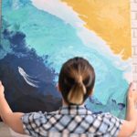 woman hangs abstract painting on wall
