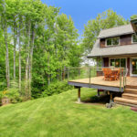 house with wooden deck on large lawn near trees