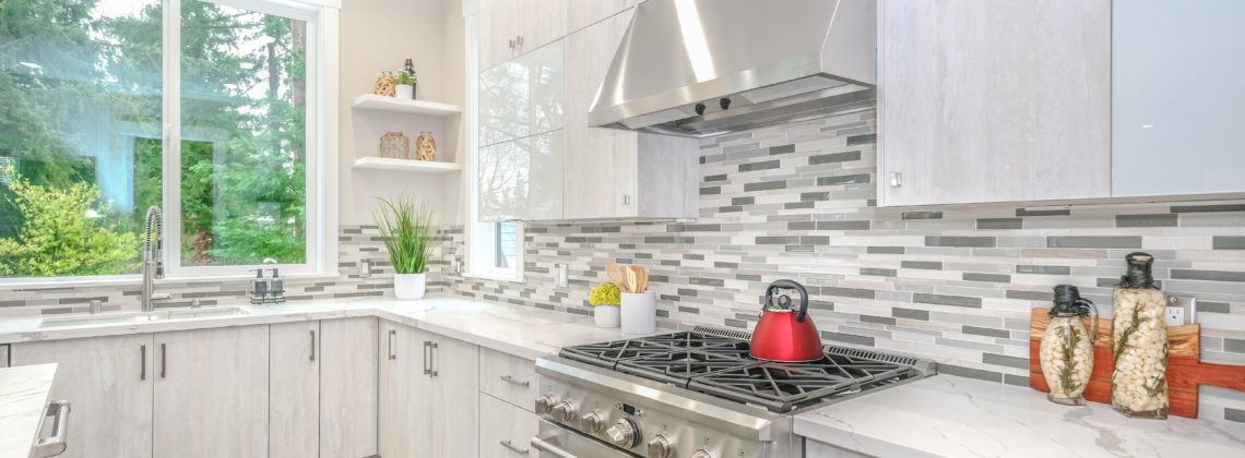 beautiful white and grey kitchen with marble countertops and a stainless steel gas stove