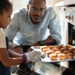 little girl pulls muffins from oven while happy father watches