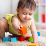 baby girl plays with colorful blocks on carpet