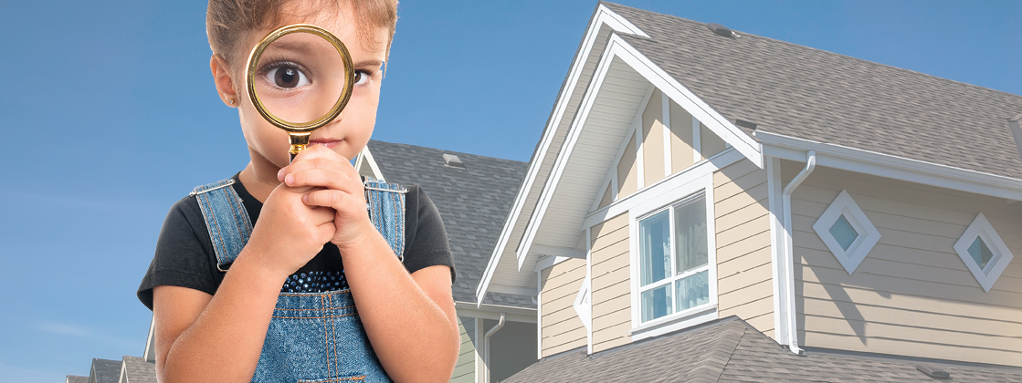 A little girl holding a magnifying glass in front of her face standing in front of a house