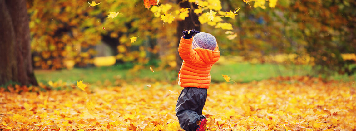 child in orange coat catches falling leaves