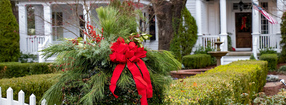red holiday bow on bushes outside a white house