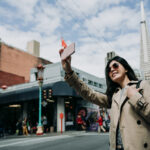 A woman holding a phone above her head in the middle of the street