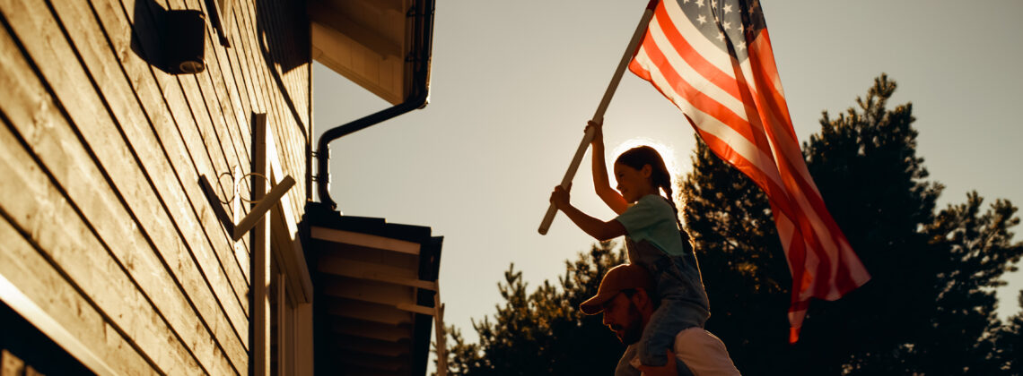 father with daughter on his shoulder putting up an American flag