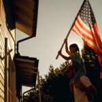 father with daughter on his shoulder putting up an American flag