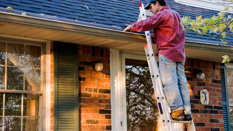 Man on a ladder cleaning gutters