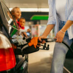 Woman pumping gas into her car while her children look on from the window