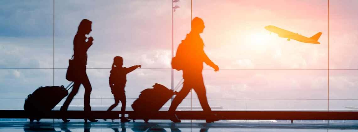 family walking through the airport with luggage while plane takes off